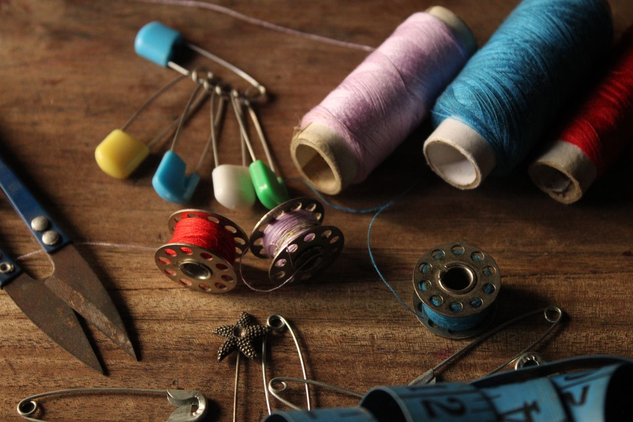 Sewing accessories include threads, scissors, and bobbins on a wooden table.