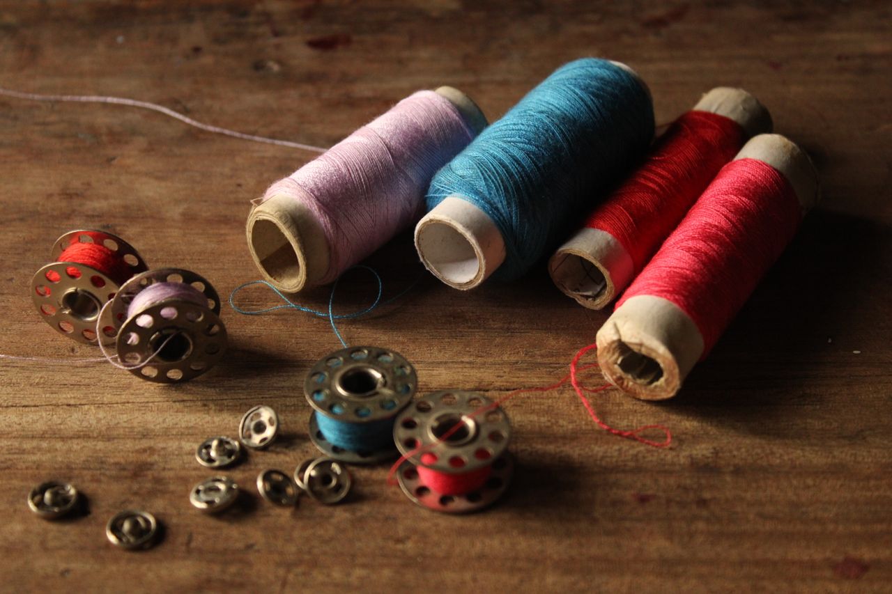 A collection of colorful sewing threads and metal bobbins on a rustic wooden table, ideal for crafting projects.
